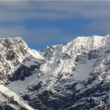 An impressive mountain landscape with snow-covered peaks and a clear blue sky. The rocks are steep and majestic.