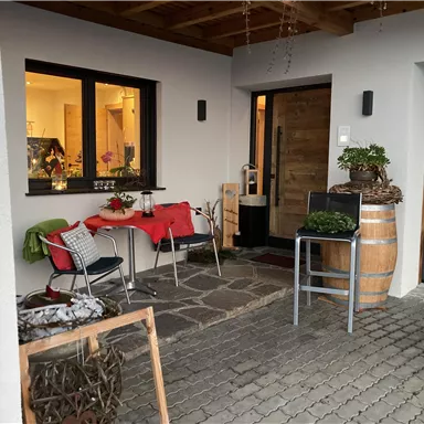 Ein einladender Eingangsbereich mit einem Tisch und Stühlen. Die Atmosphäre ist gemütlich und freundlich, perfekt für entspannte Stunden im Freien.