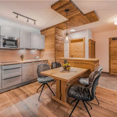 A modern kitchen with wooden cladding and a dining table. The room is bright and inviting, ideal for social meals.