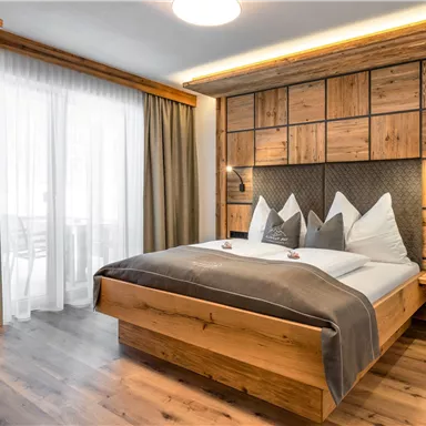A modern bedroom with wooden details and a large double bed. Large windows provide plenty of natural light.