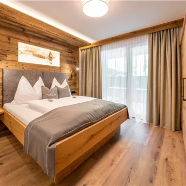 A modern bedroom with wooden paneling and a large window. It is a bright and cozy atmosphere with a comfortable bed.