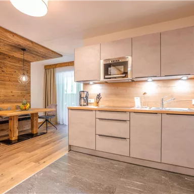 A modern kitchen with wooden details and a cozy dining area. The light highlights the simple, elegant lines of the space.