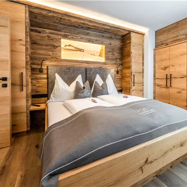 A modern bedroom with a large bed and wooden furniture. The walls are paneled with wood, and there are gray accents.