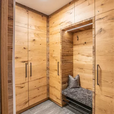 A modern entrance area with wooden cabinets and a cozy seating nook. The walls are made of light wood, and the floor is tiled with gray tiles.