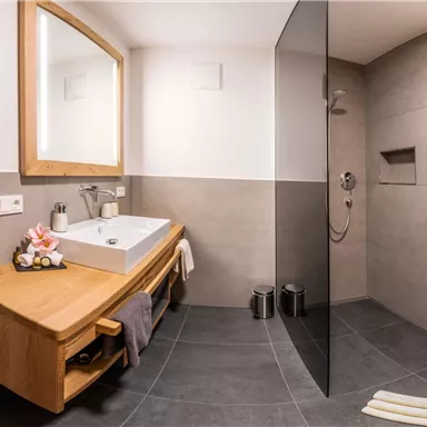 A modern bathroom with a large shower and a wooden sink. The walls are in neutral tones and there is a mirror above the sink.