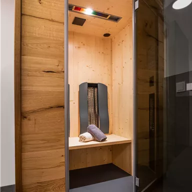 A modern infrared cabin made of wood with a bench and a towel. The walls are light and create a relaxing atmosphere.