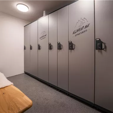 A modern changing room with several gray lockers. The walls are simple and the floor is made of gray material.