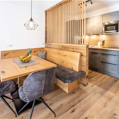 A modern dining room with a wooden table and comfortable chairs. The open kitchen is well-equipped and offers a cozy atmosphere.