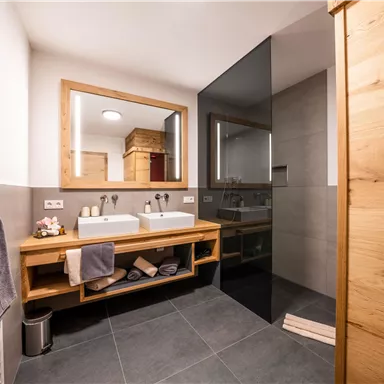 Elegant bathroom with two wash basins, wooden shelf, and modern shower. The combination of wood and neutral colors creates a pleasant atmosphere.