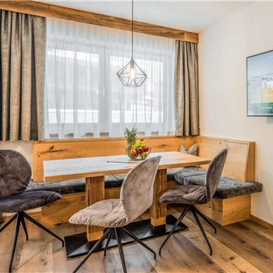 A modern dining room with a wooden table and upholstered chairs. Large windows let in plenty of light, and an elegant ceiling lamp provides stylish illumination.