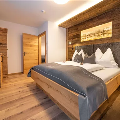 A modern bedroom with a large wooden bed and elegant furnishings. The walls are panelled with wood, and there is soft lighting.