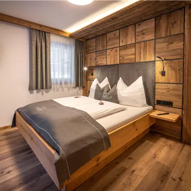 A modern bedroom with wood decor and a large double bed. The atmosphere is cozy and inviting, with soft lighting and a television on the wall.