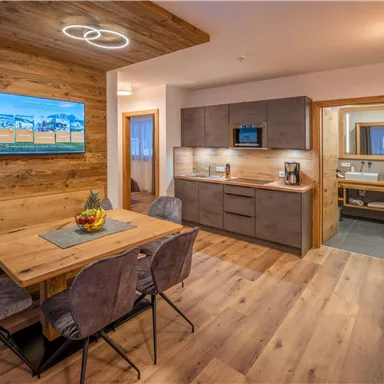 A modern kitchen with a wooden dining table and stylish chairs. The room has a warm atmosphere with wooden walls and soft lighting.