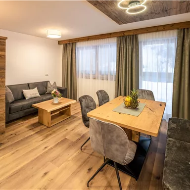 A cozy living space with a modern couch and a wooden table. Large windows let in plenty of light and create an inviting atmosphere.