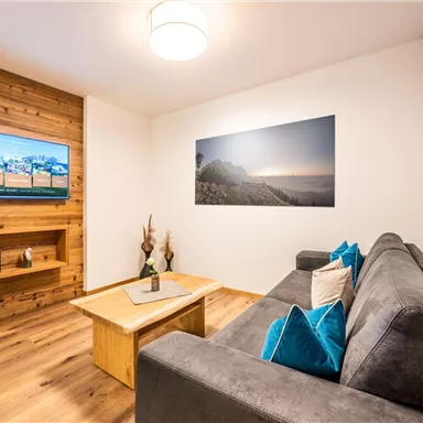 A modern living room with a comfortable sofa and a wooden shelf. A large picture hangs on the wall, and a television stands on a wooden stand.