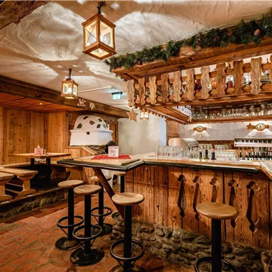 Eine gemütliche Bar mit Holzinterieur und warmem Licht. Tische und Stühle laden zum Verweilen ein.