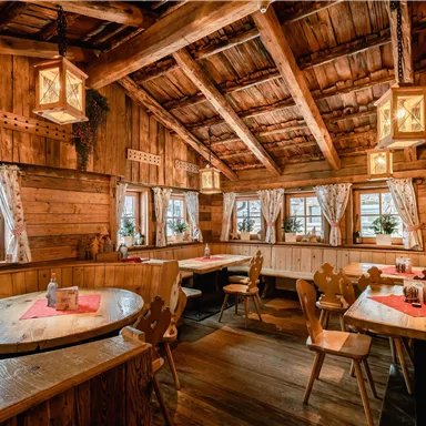Ein gemütliches Restaurant mit Holzwänden und rustikalem Dekor. Der Raum verfügt über runde Tische und Fenster mit Vorhängen.