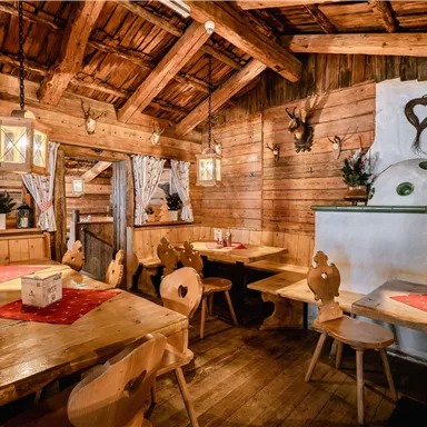 Ein gemütliches Restaurant mit Holzmöbeln und traditioneller Dekoration. Die Wände sind aus Holz, und es gibt viele rustikale Details wie Laternen und Geweihe.