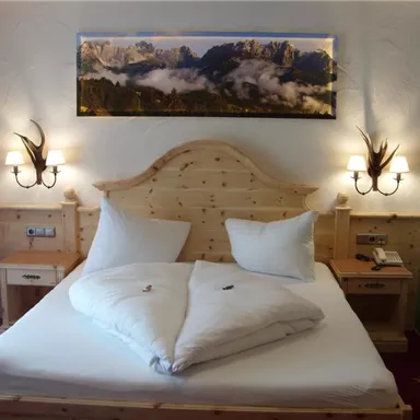Ein gemütliches Schlafzimmer mit einem Holzbett und zwei großen Kopfkissen. An der Wand hängt ein Bild von Bergen, und es gibt Nachttische mit Lampen.