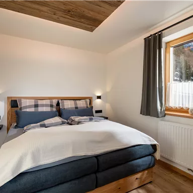 Ein modernes Schlafzimmer mit einem großen Bett und ansprechender Holzdecke. Das Fenster bietet einen Blick auf die Berge und lässt viel Tageslicht herein.
