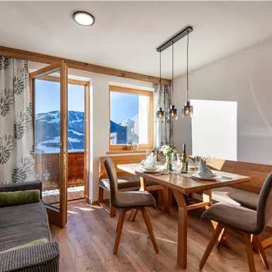 Ein gemütlicher Essbereich mit Holztafel und Stühlen, umgeben von großen Fenstern mit Blick auf die Berge. Das moderne Wohnzimmer verfügt über eine bequeme Couch und stilvolle Beleuchtung.