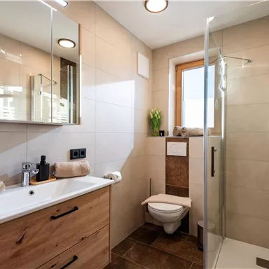 Ein modernes Badezimmer mit einer Dusche und hellen Fliesen. Die Ausstattung umfasst ein Holzwaschbecken und große Spiegel.