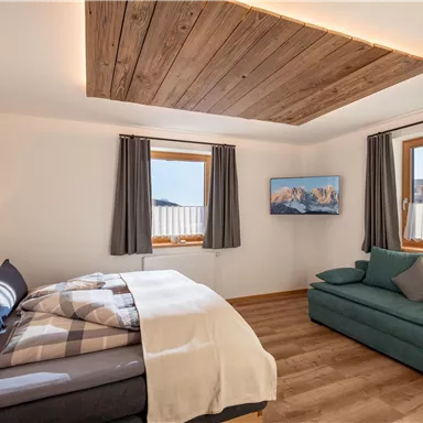 Ein geräumiges, modernes Schlafzimmer mit einem Doppelbett und einem gemütlichen Sofa. Große Fenster bieten einen Blick auf die Landschaft.