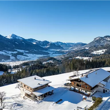 Eine verschneite Landschaft mit zwei charmanten Häusern und majestätischen Bergen im Hintergrund. Der klare Himmel und die unberührte Natur schaffen eine friedliche Atmosphäre.