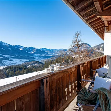 Ein schöner Balkon mit Blick auf schneebedeckte Berge und ein klarer blauer Himmel. Entspannte Sitzmöglichkeiten laden zum Verweilen ein.