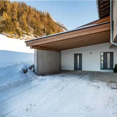 A modern building with a covered entrance in a snowy landscape. Forested hills can be seen in the background.