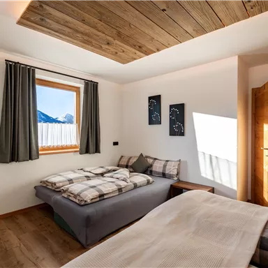 Ein modernes Schlafzimmer mit Holzdecke und großen Fenstern. Es gibt zwei Betten mit karierten Bettwäsche und eine gemütliche Atmosphäre.