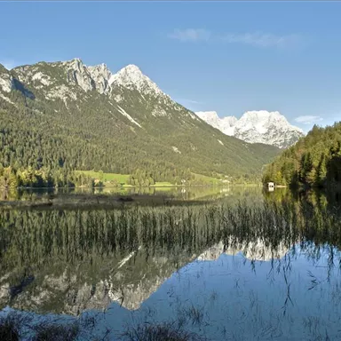 Ein schöner See, umgeben von hohen Bergen und Wäldern. Das Wasser spiegelt die Landschaft wider und bietet eine ruhige Atmosphäre.