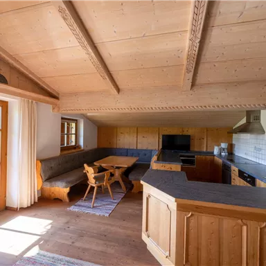 Eine gemütliche Küche mit Holzverkleidung und einem großen Essbereich. Viel natürliches Licht strahlt durch die Fenster und schafft eine einladende Atmosphäre.