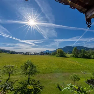 Eine weite, grüne Landschaft unter einem strahlend blauen Himmel. Die Sonne scheint hell und es sind einige Wolkenstreifen zu sehen.