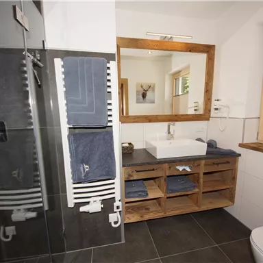 Ein modernes Badezimmer mit einer großen Dusche und einem Holzwaschtisch. Handtücher hängen ordentlich auf einem Handtuchhalter, und ein Spiegel reflektiert das helle Raumdesign.