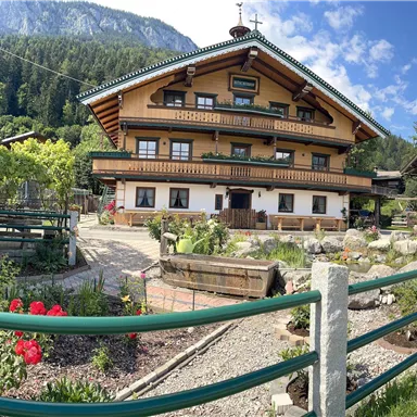 Ein traditionelles alpenländisches Haus mit Holzverkleidung und blühendem Garten.
