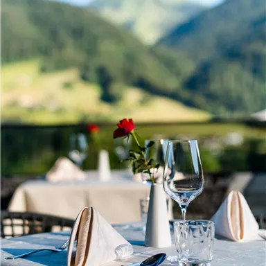 An elegantly set table with a view of the mountains. A rose is on the table and glasses are ready for enjoyment.