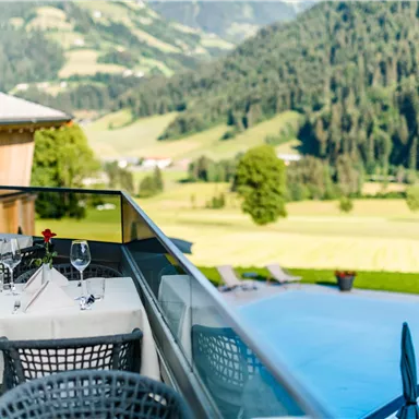 A beautiful outdoor area of a restaurant with covered tables and a view of a green landscape. In the background, mountains and a blue pool are visible.