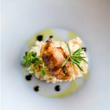 Ein kunstvoll angerichtetes Gericht mit cremigem Risotto und einer gegrillten Köstlichkeit obendrauf. Frische Kräuter und eine Balsamico-Reduktion verleihen dem Gericht eine besondere Note.