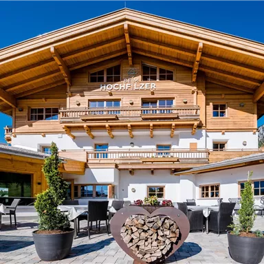 A charming wooden building in alpine style with a large porch.
Patio furniture and plants invite you to linger.