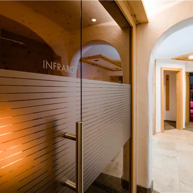 Ein moderner Spa-Bereich mit einem gläsernen Eingang zu einem Infrarotraum. Die Wände sind hell und freundlich, mit gemütlicher Beleuchtung im Hintergrund.