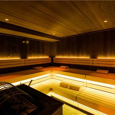 Ein modernes Sauna-Interieur mit warmem, sanftem Licht. Die Holzverkleidung und die Bänke schaffen eine entspannende Atmosphäre.