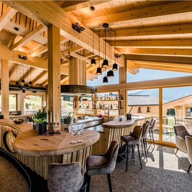 Ein modernes Restaurant mit Holzkonstruktion und großen Fenstern. Der Raum ist hell und einladend, mit einer zentralen Bar und stilvollen Sitzgelegenheiten.