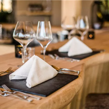 Ein eleganter Tisch gedeckt mit Servietten und Gläsern in einem modernen Restaurant. Die Holzoberfläche und die stilvolle Dekoration schaffen eine einladende Atmosphäre.