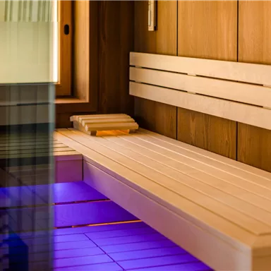 Eine moderne Sauna mit Holzverkleidung und sanfter Beleuchtung. Die Bänke bieten Platz zum Entspannen und Wohlfühlen.