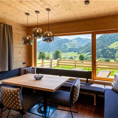 Ein gemütlicher Essbereich in einem Holzhaus mit Blick auf die grünen Berge. Große Fenster lassen viel Licht herein und bieten eine schöne Aussicht auf die Landschaft.