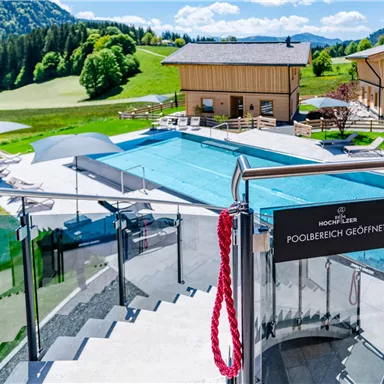 A beautiful pool area surrounded by green meadows and mountains. The wooden houses provide an inviting atmosphere for visitors.
