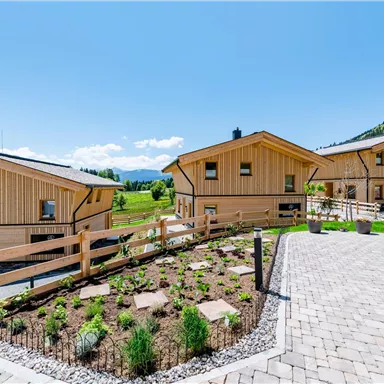 Two modern wooden chalets in a picturesque mountain landscape. The garden is well-kept and the surroundings are bright and inviting.