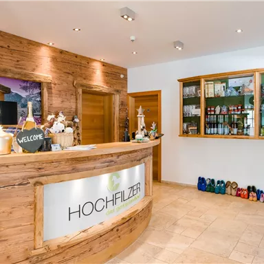 Eine moderne Empfangshalle mit einem Holzthekenbereich. Im Hintergrund sind Regale mit Getränken und farbigen Schuhen zu sehen.