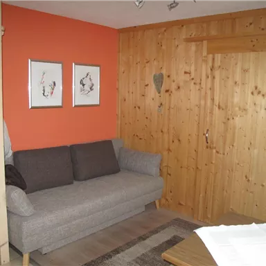 A cozy living room with a gray sofa and wooden-paneled walls. Two pictures and a wooden heart hang on the wall.